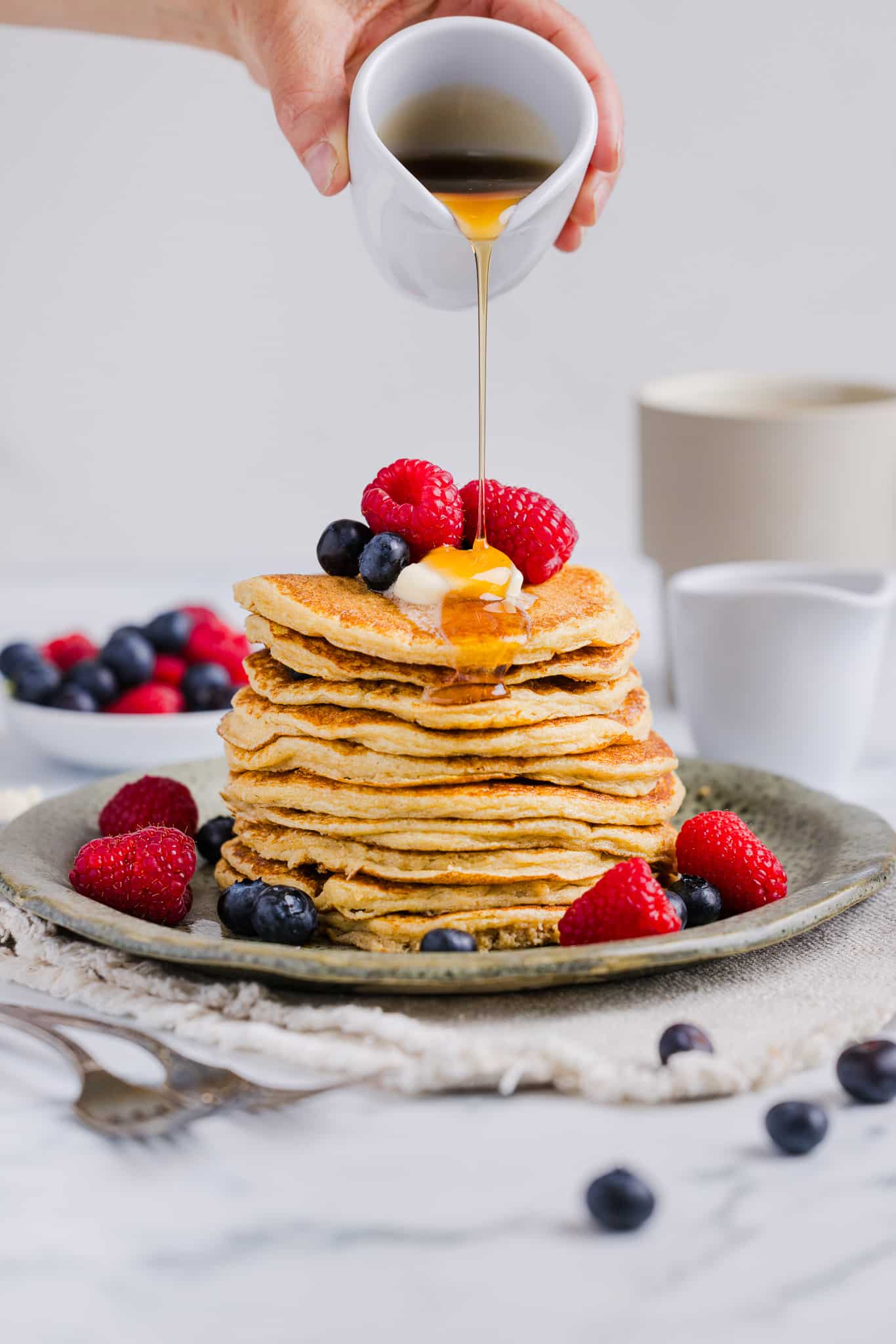 Oatmeal cottage cheese pancakes on a plate with berries and maple syrup.
