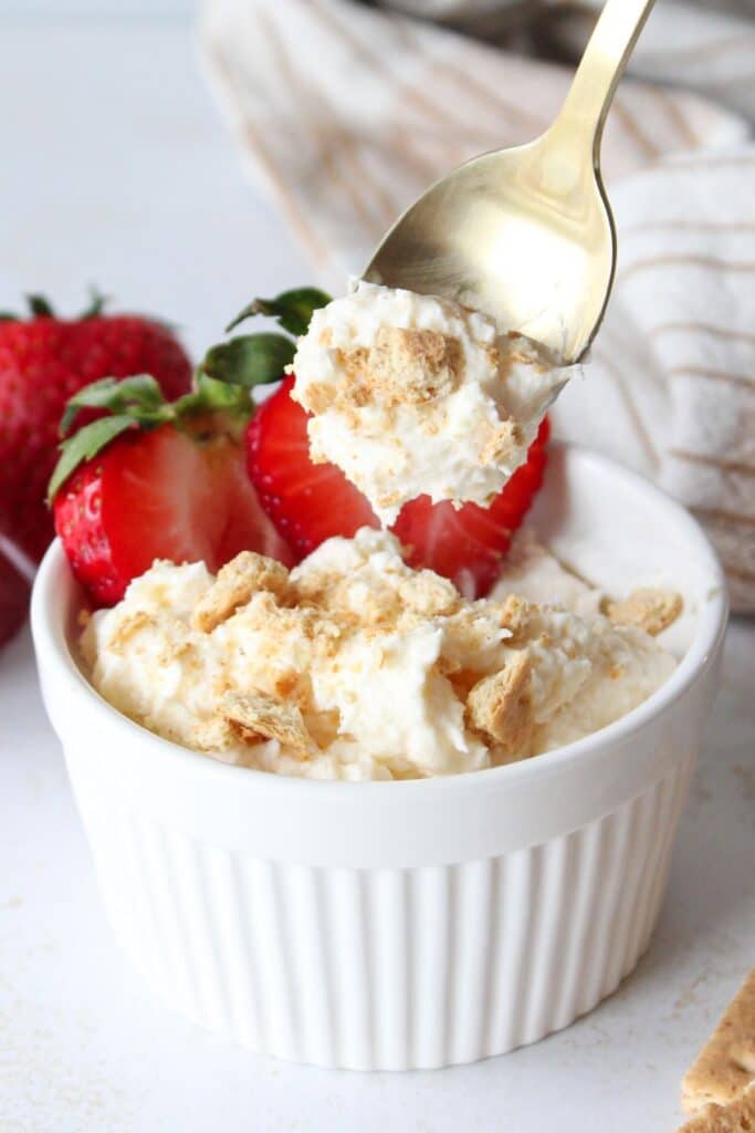 A spoonful of cheesecake fluff and a bowl of cheesecake fluff with strawberries.
