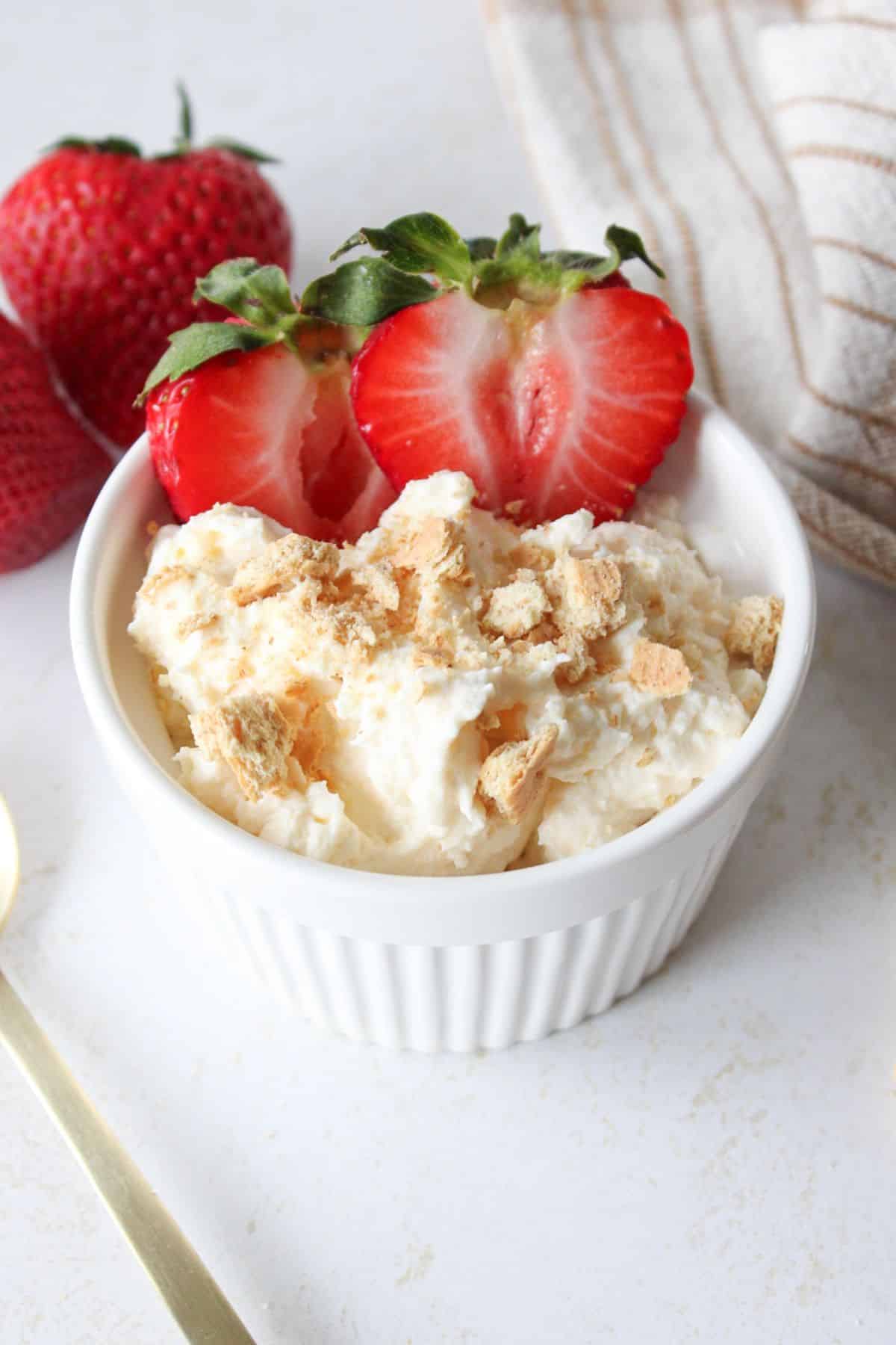 Cheesecake fluff in a white bowl with graham cracker crumbs and sliced strawberries.