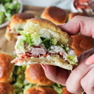 A hand holding up a chopped italian sliders with many sliders in the background.