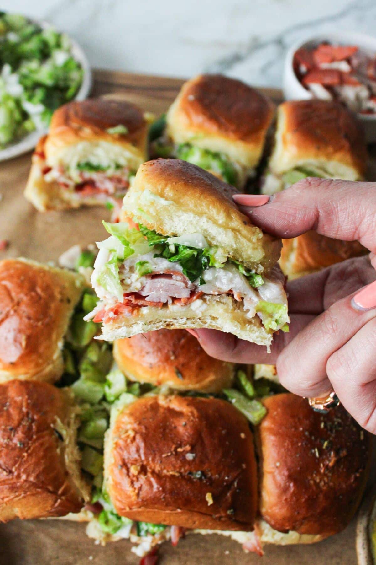 A hand holding up a chopped italian sliders with many sliders in the background.