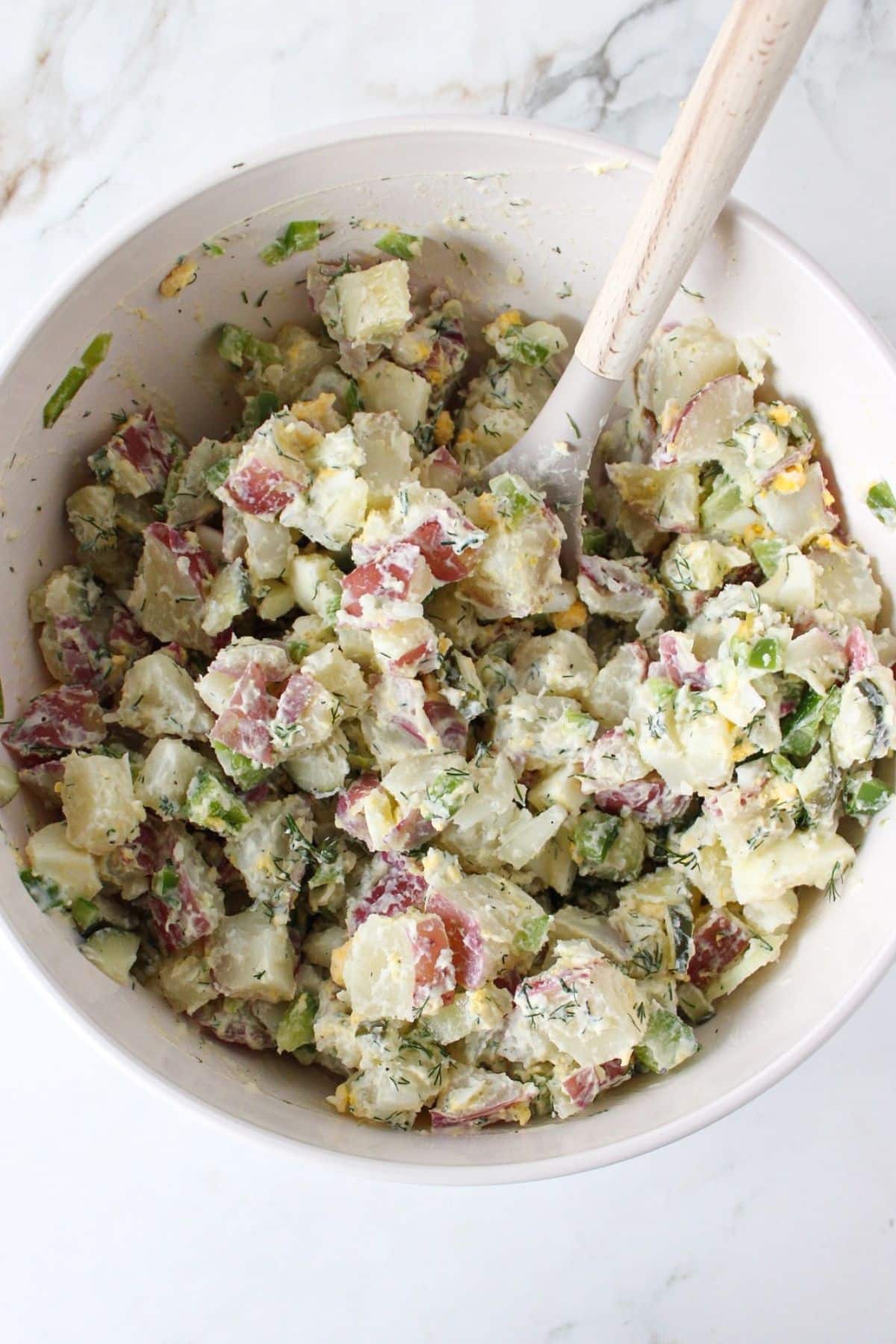 Dill pickle potato salad mixed in a white bowl.