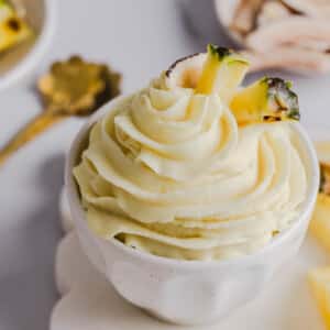 The dole whip in a white bowl garnished with pineapple on a white countertop.