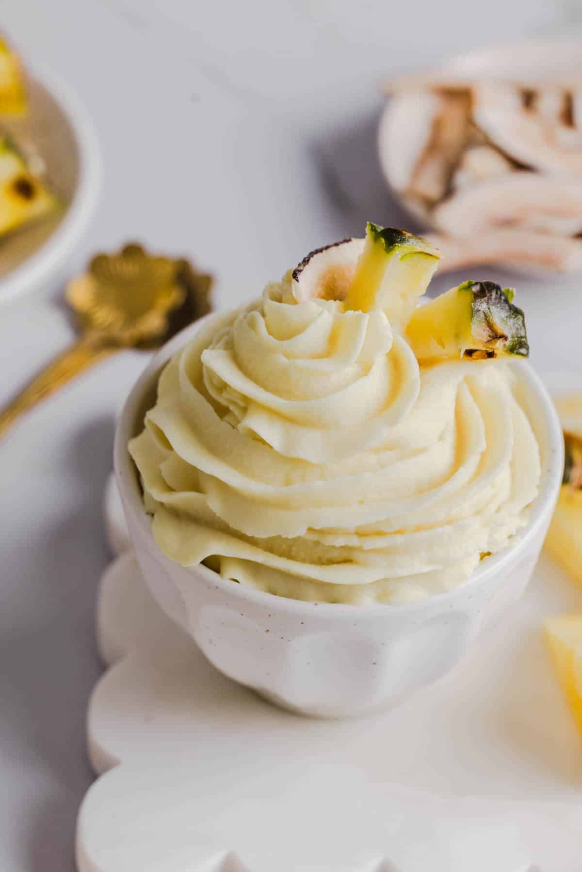 The dole whip in a white bowl garnished with pineapple on a white countertop.