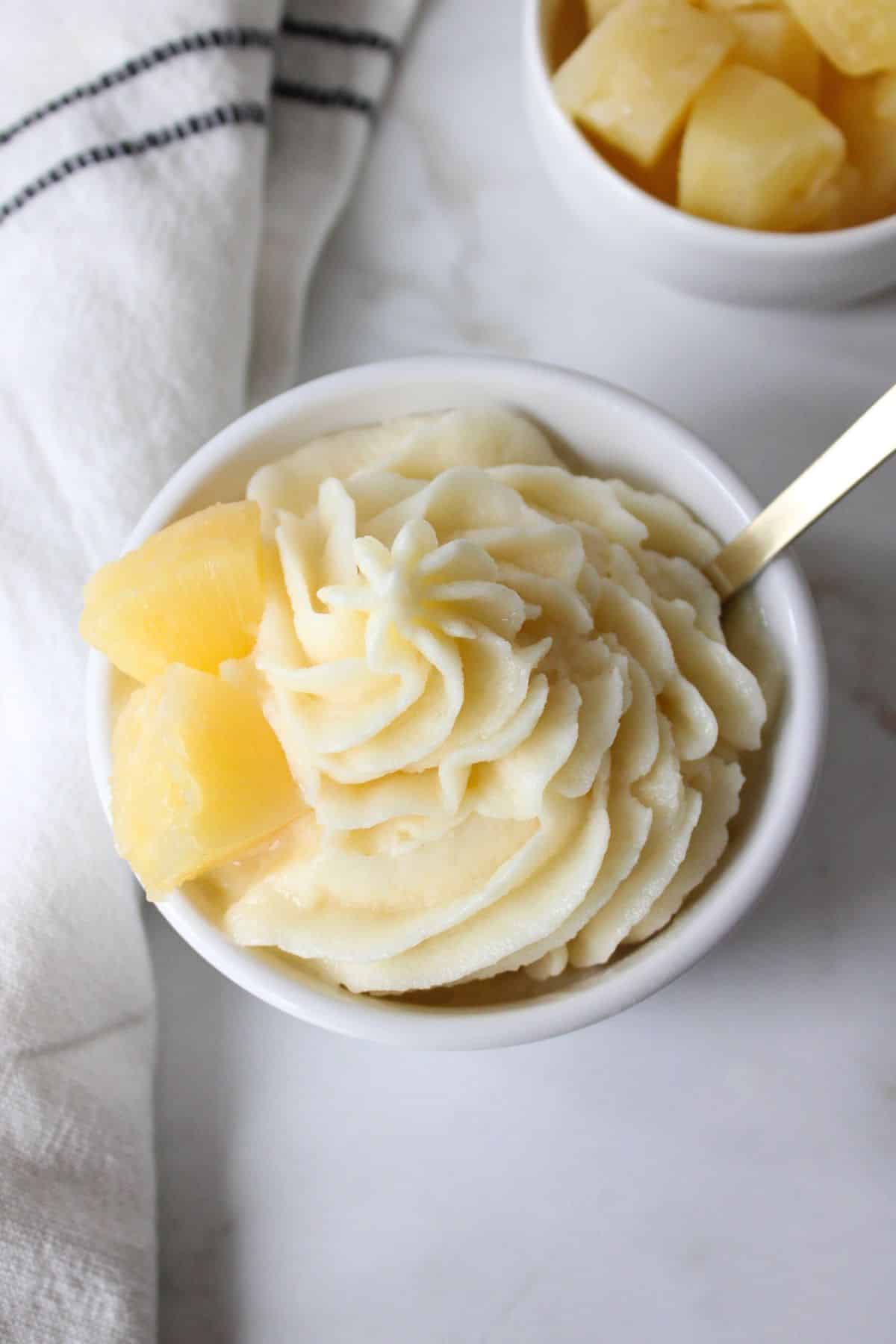 Dole whip made in the Ninja creami in a white bowl with pineapple and a spoon.