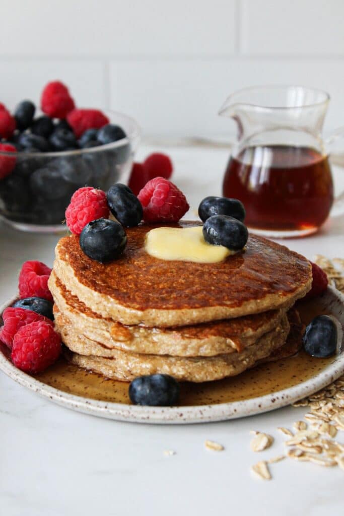 Oatmeal cottage cheese pancakes on a plate with berries and maple syrup.