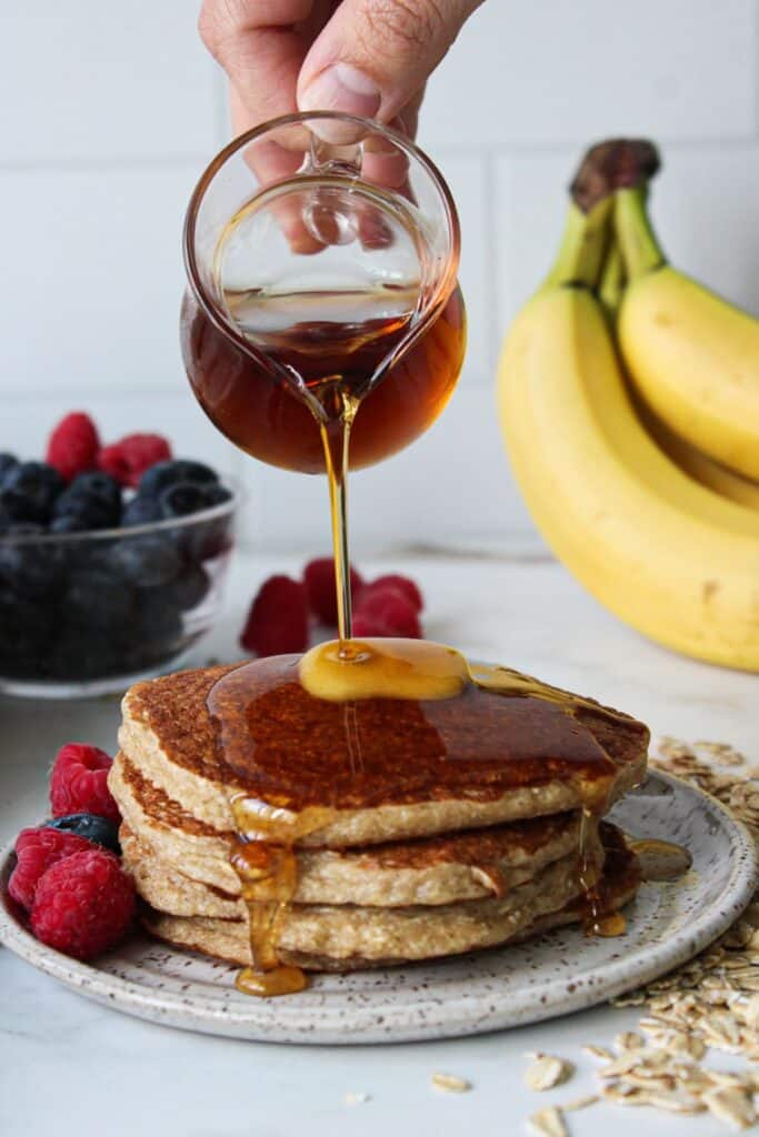 Maple syrup being poured onto a stack of oatmeal cottage cheese pancakes.