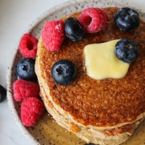 Oatmeal cottage cheese pancakes on a plate with berries and maple syrup.
