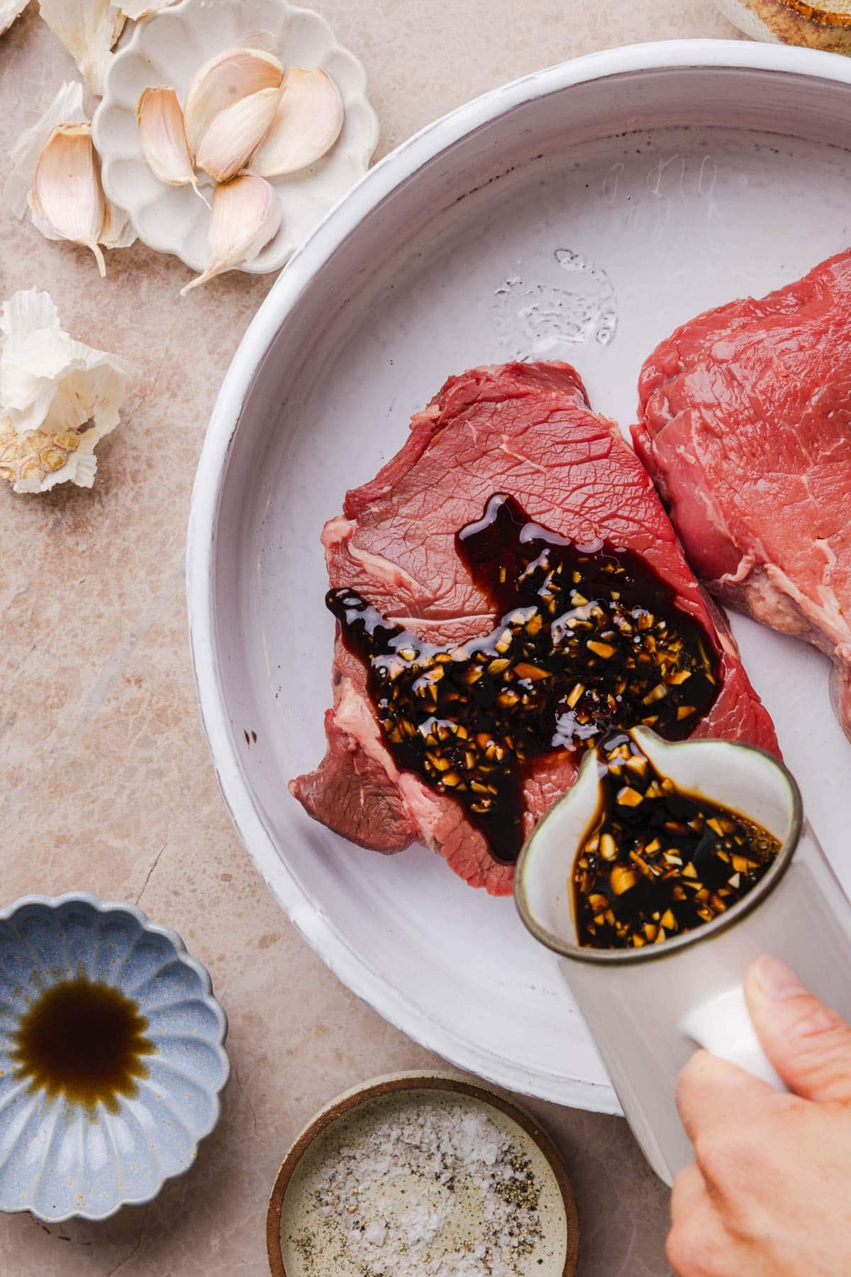 Pouring the marinade over a piece of steak in a shallow bowl.