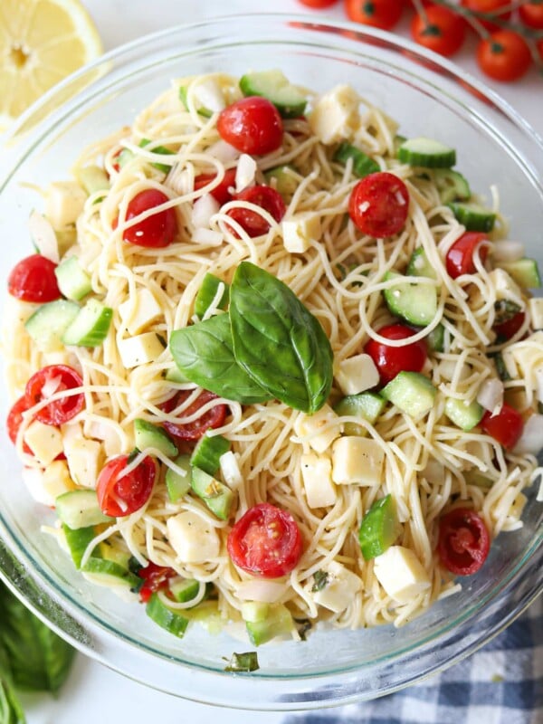 Angel hair pasta salad in a large glass bowl garnished with fresh basil.
