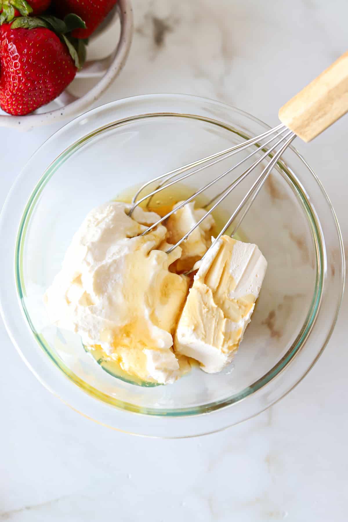 Ingredients for deviled strawberries in a glass bowl with a whisk.