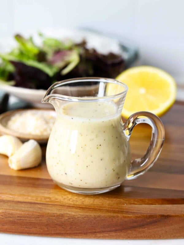Garlic parmesan dressing in a glass container with garlic and lemon on a wooden board.