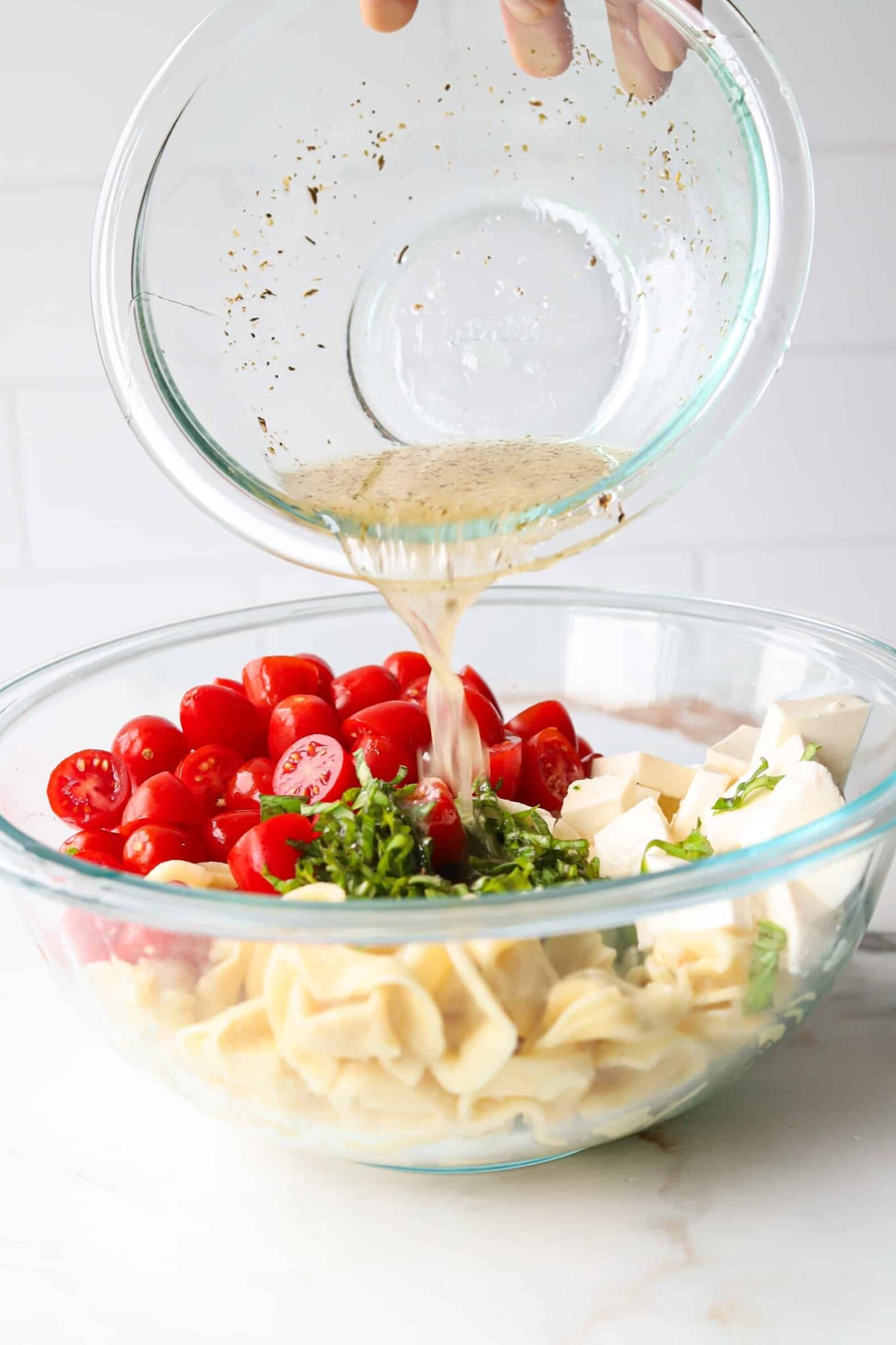 White balsamic dressing being poured on ingredients for Caprese tortellini salad.