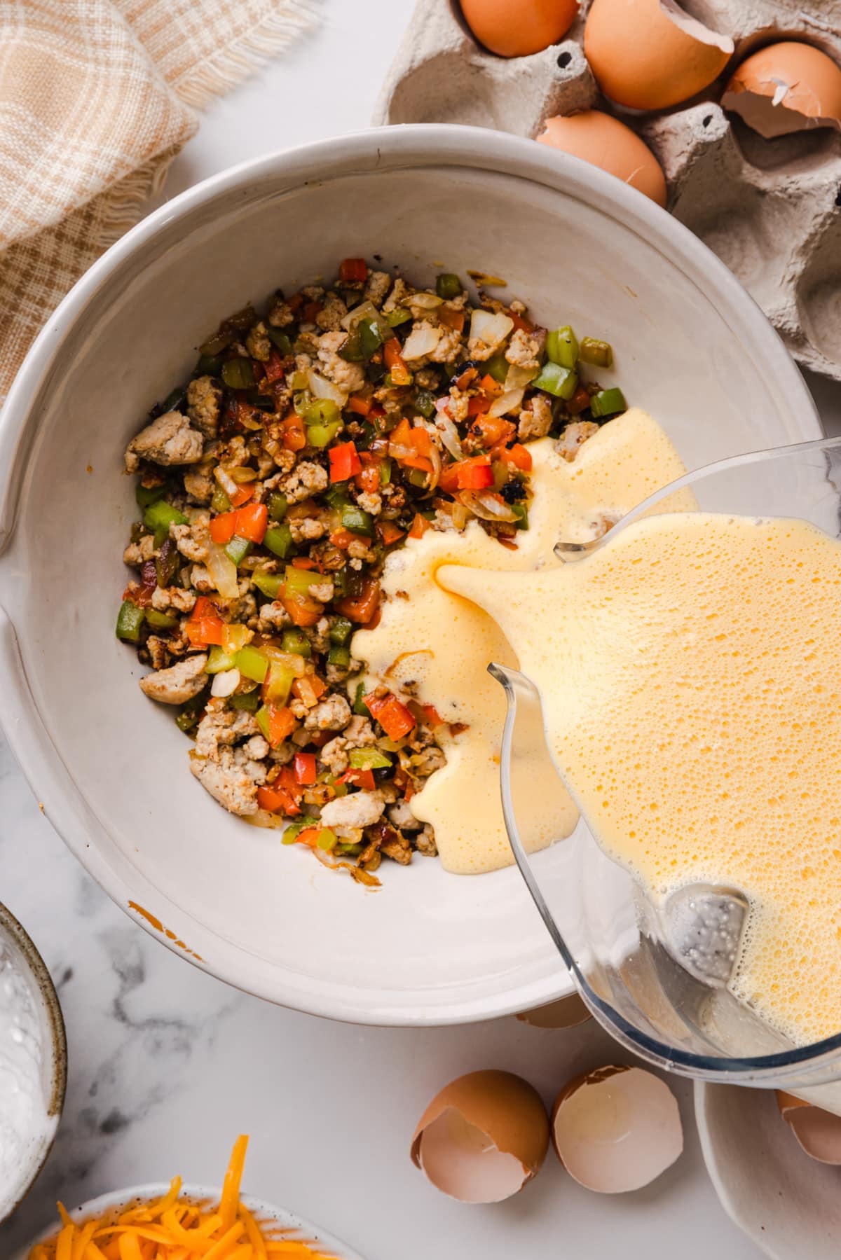 The egg and cottage cheese mixture is pouring into a bowl with the cooked sausage, peppers, and onions.
