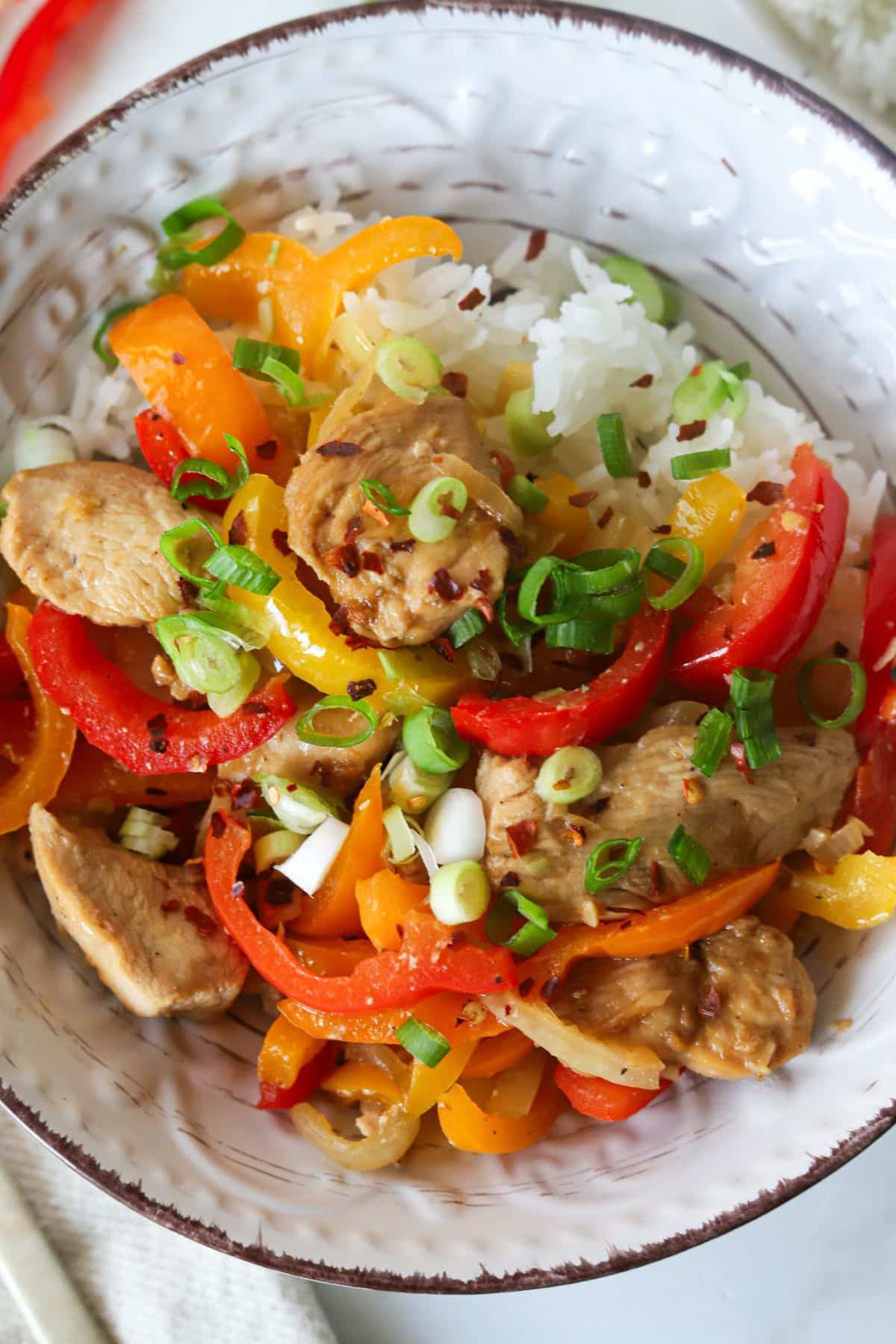 Chicken with peppers and onions stir fry topped with green onions and served with rice.