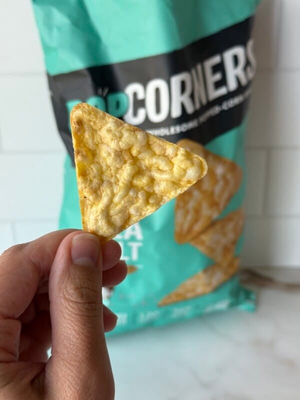 A hand holding up a PopCorners chip.