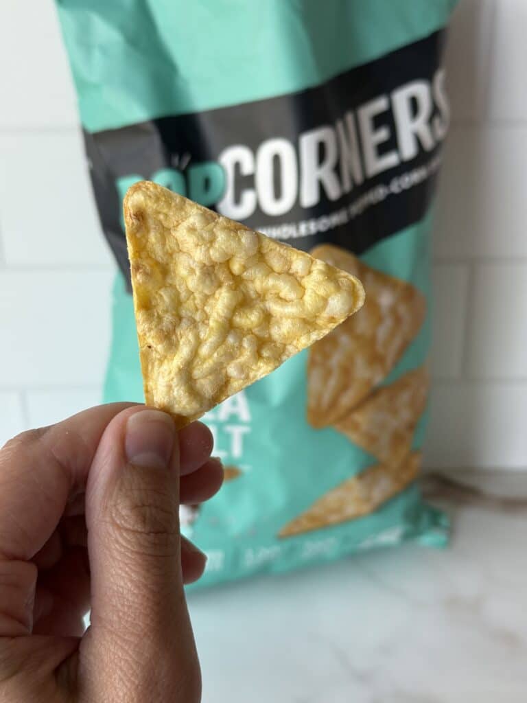 A hand holding up a PopCorners chip.