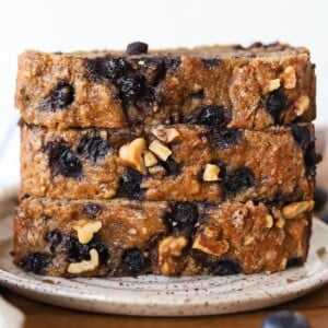 Three slices of banana nut bread with blueberries stacked on a plate.