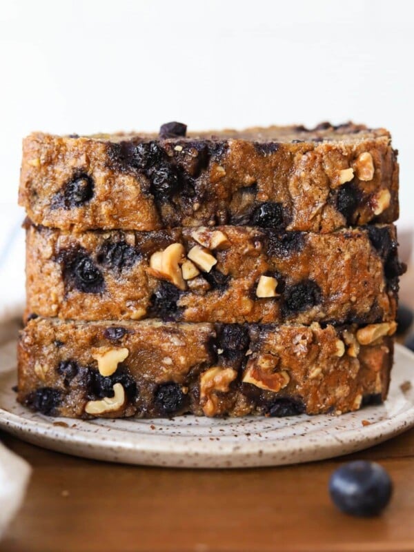 Three slices of banana nut bread with blueberries stacked on a plate.