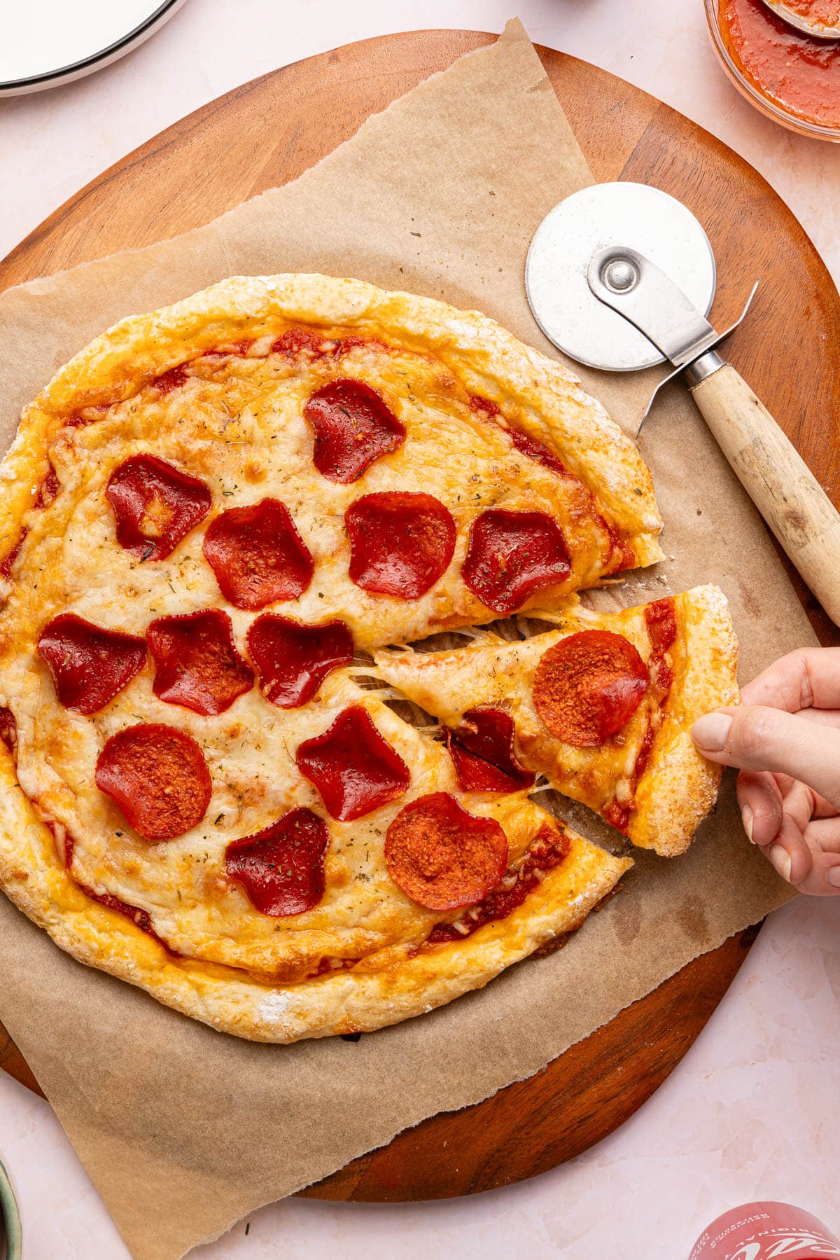 A hand removes a slice of pizza from the cottage cheese pizza sitting on a piece of parchment paper on top of a wooden cutting board.