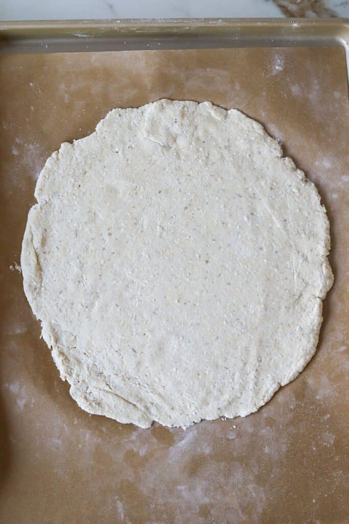 Cottage cheese pizza crust dough rolled out on parchment paper.