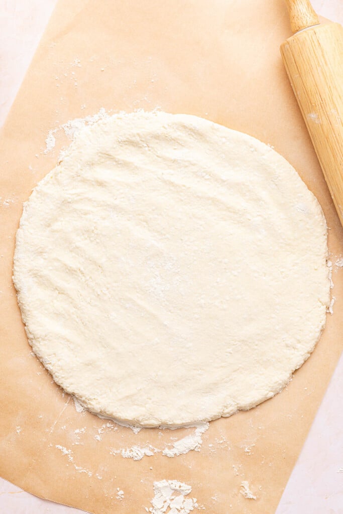 The pizza dough rolled into a round circle on the piece of parchment paper.