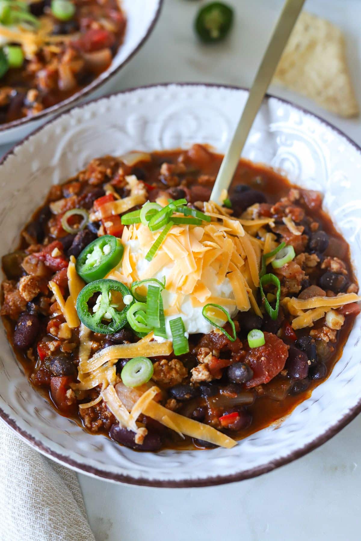 Ground chicken chili recipe topped with sour cream, cheddar cheese and jalapeños.