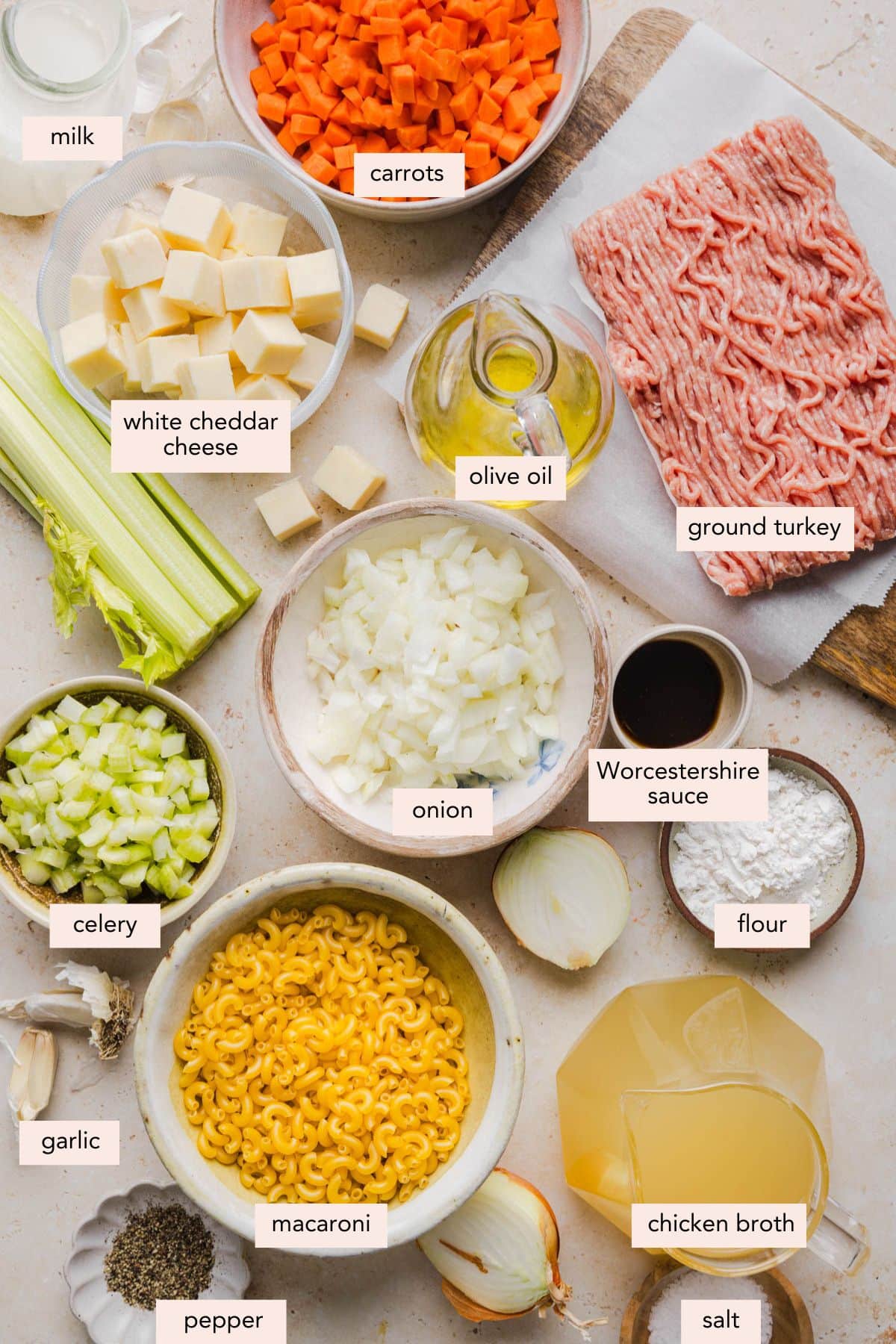 All of the ingredients for cheeseburger macaroni soup in bowls on a white countertop.