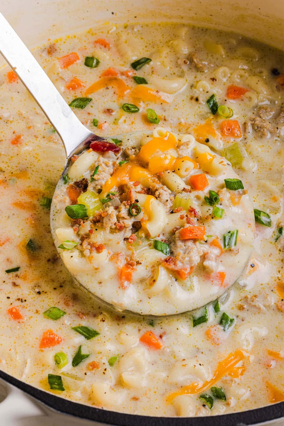 A ladle scoops up the finished cheeseburger macaroni soup from the pot for serving.