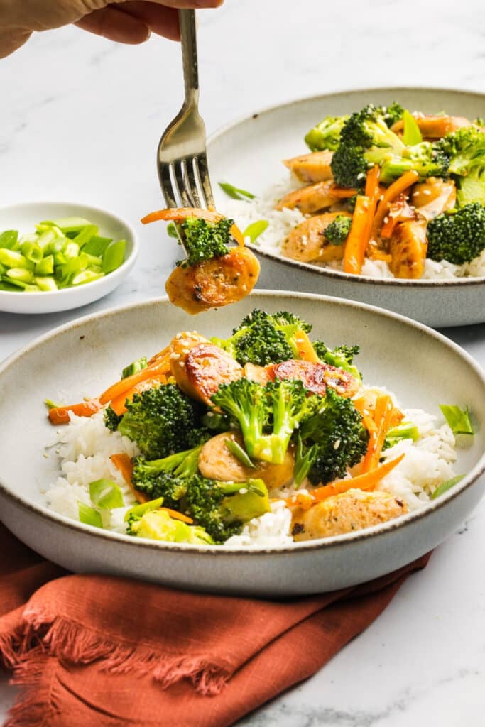A fork picking up a bite of chicken sausage broccoli stir-fry.