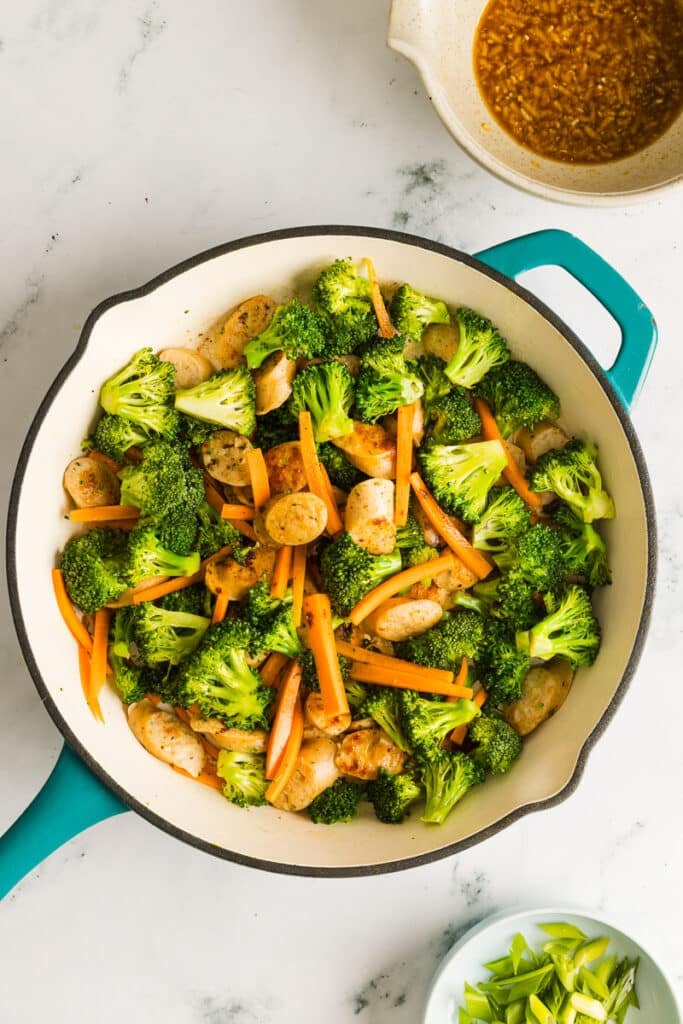 Broccoli and carrots added to a pan with chicken sausage.