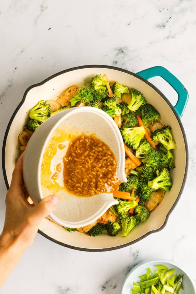 Honey garlic sauce being added to a stir fry with broccoli and chicken sausage.