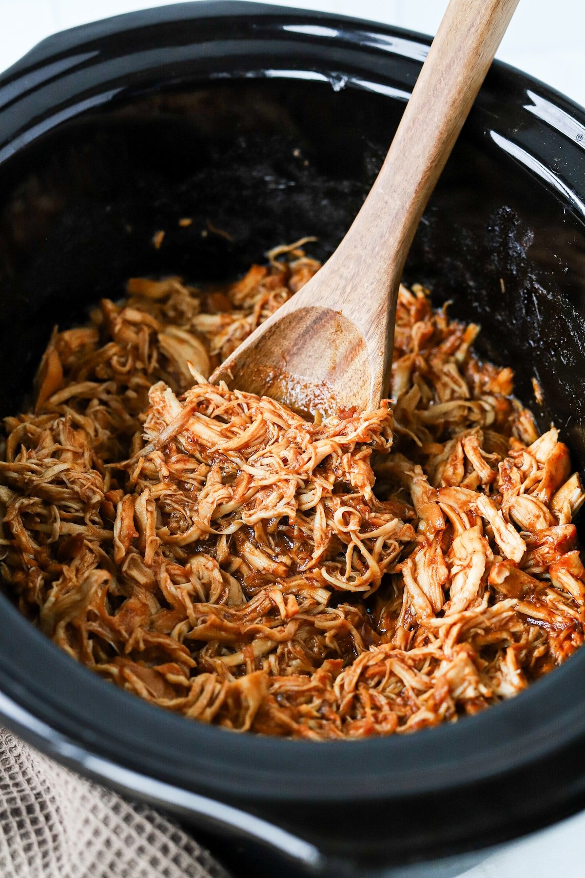 Brown sugar BBQ chicken in a slow cooker with a wooden spoon.