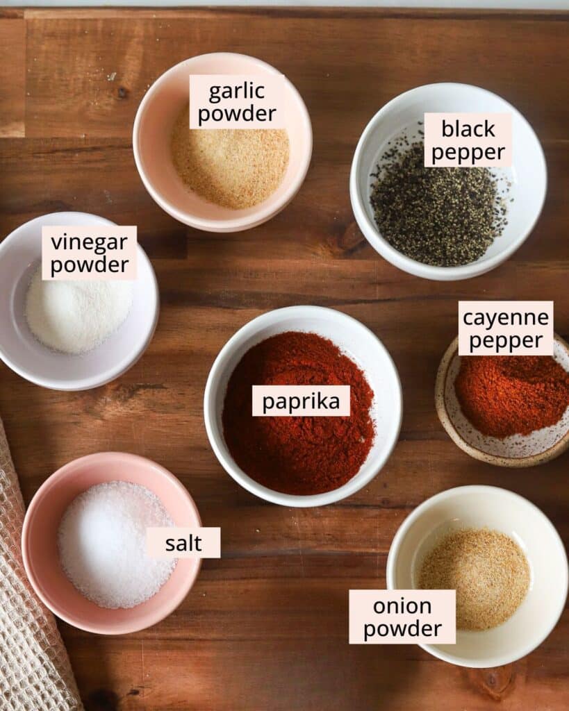 Buffalo chicken dry rub spice ingredients in small bowls with labels on a wooden board.