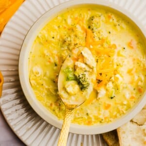 A bowl of chicken broccoli cheddar soup with a hand holding the spoon.