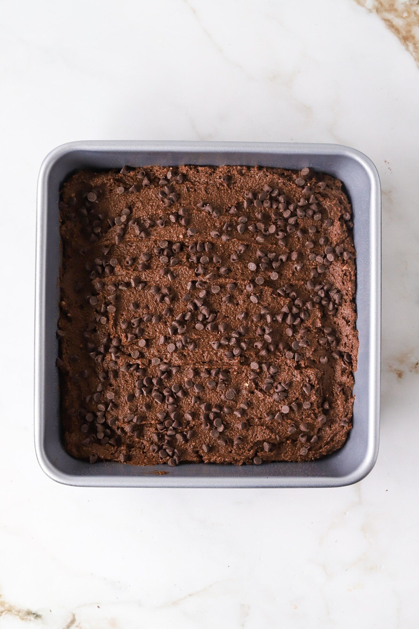 Cottage cheese brownie batter in a pan topped with mini chocolate chips.