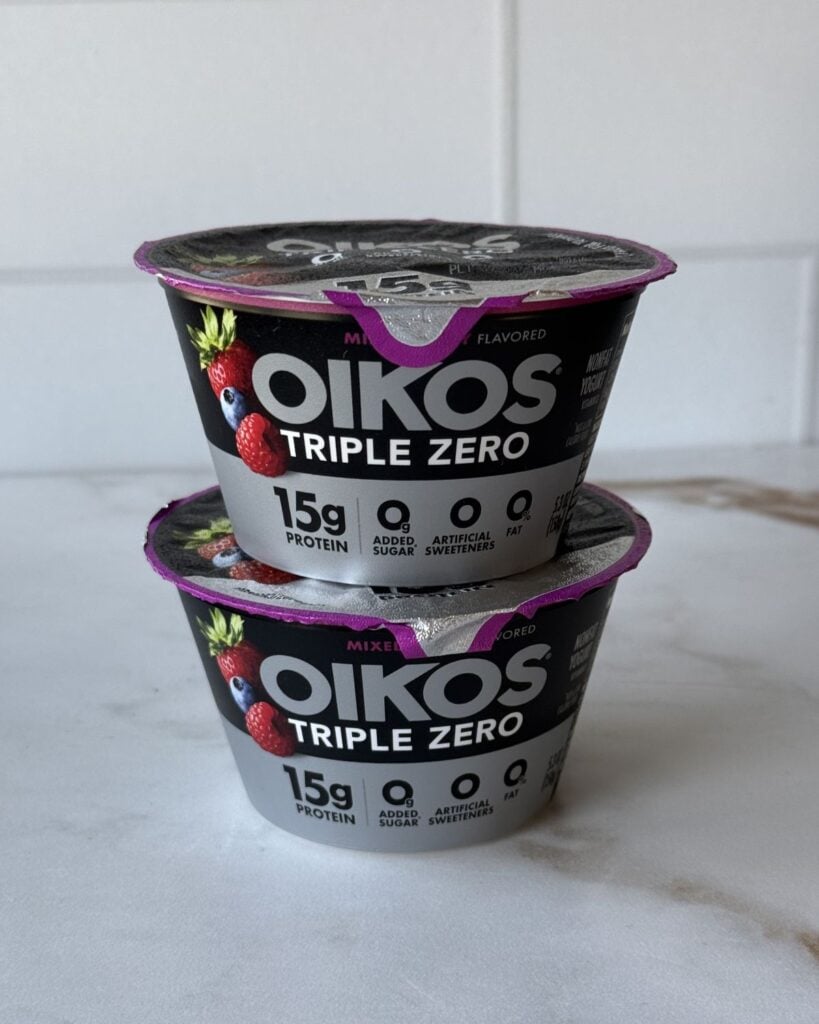 Two stacked berry Oikos triple zero yogurts on a countertop.
