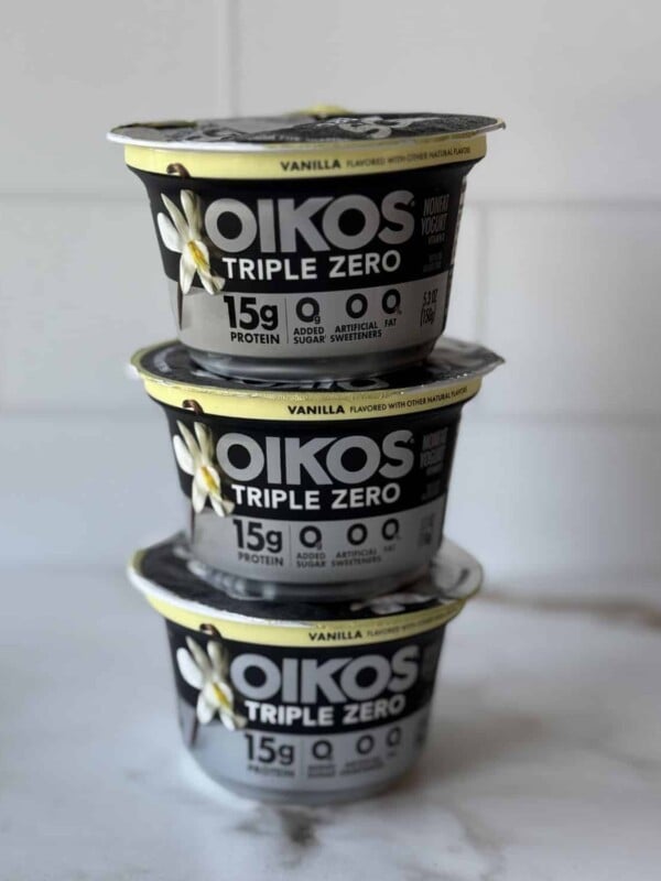 Three stacked vanilla Oikos triple zero yogurts on a countertop.
