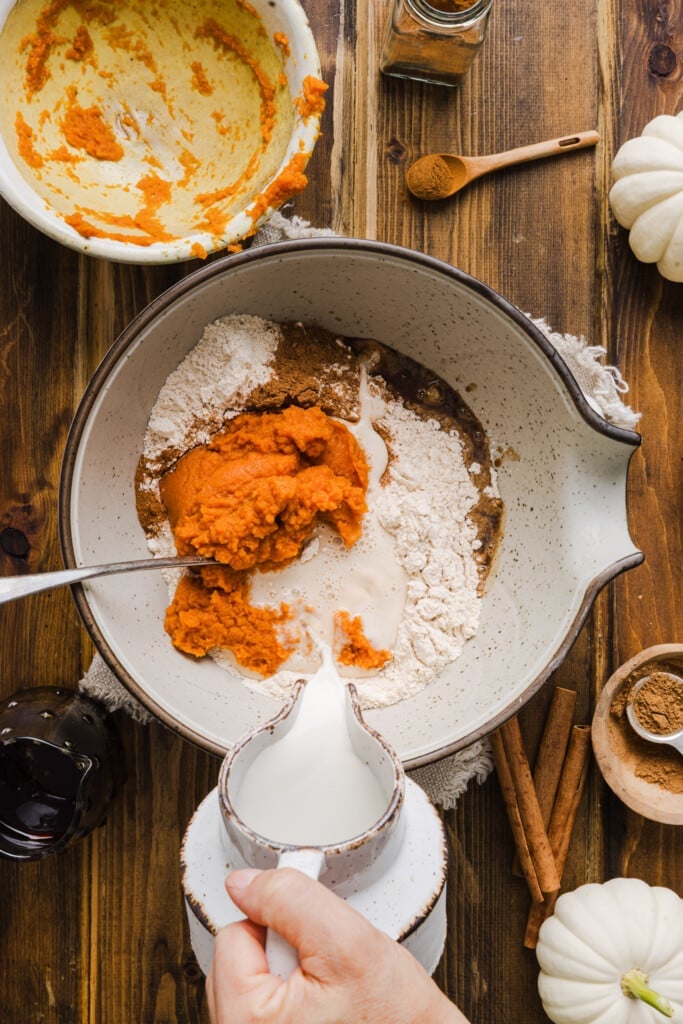Ingredients for pumpkin pancakes with pancake mix being added to a large bowl.