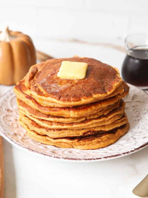 Pumpkin pancakes stacked on a plate with butter.