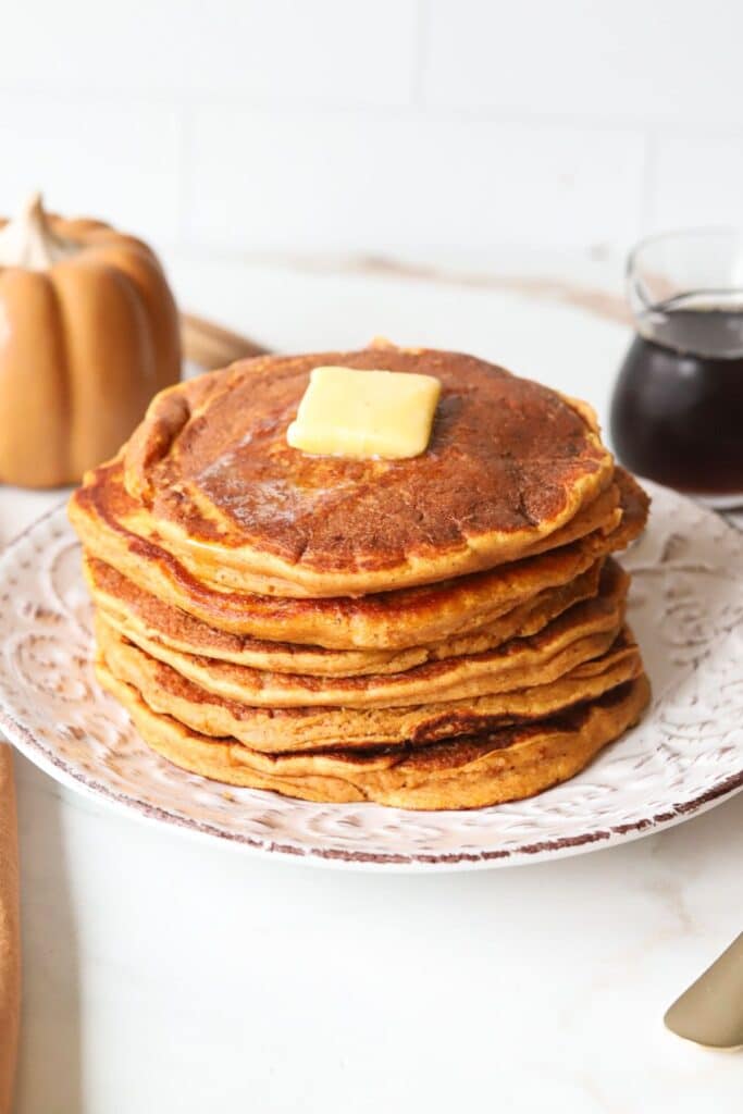 Pumpkin pancakes stacked on a plate with butter.