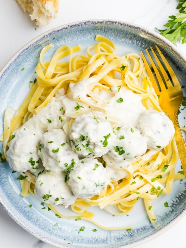 Alfredo meatballs on a plate with pasta and garnished with parsley.