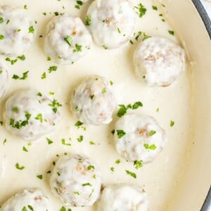 Chicken meatballs in alfredo sauce in a pan garnished with finely chopped parsley.
