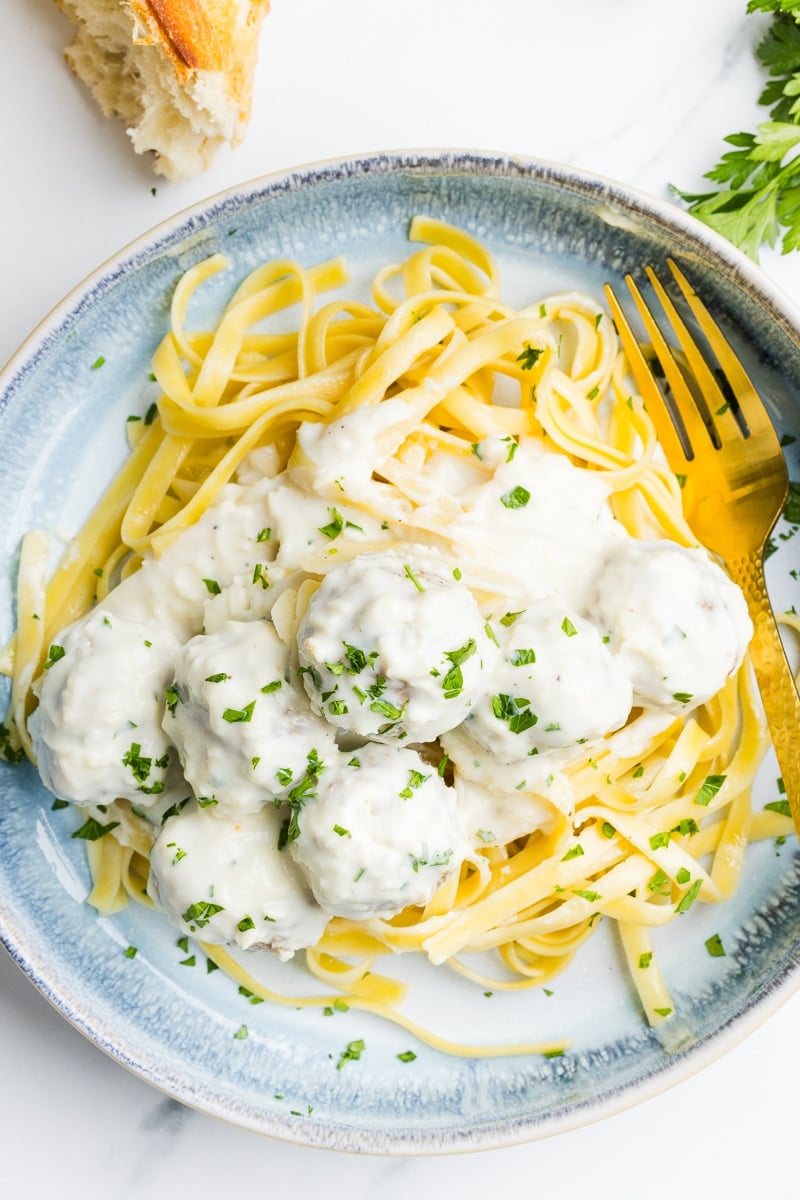 Alfredo meatballs on a plate with pasta and garnished with parsley.
