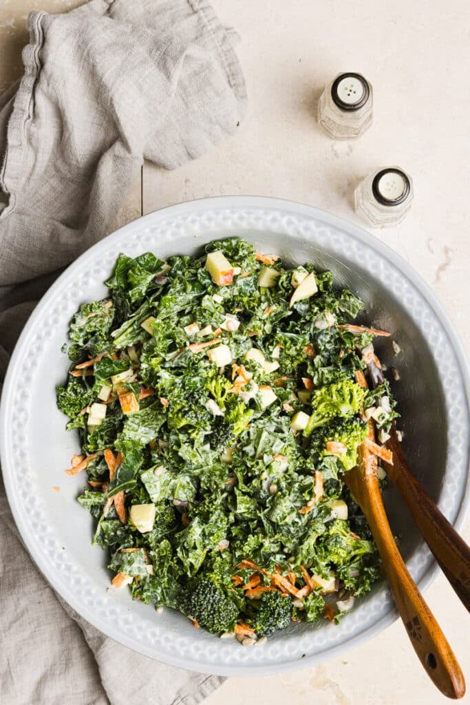 Kale and broccoli salad mixed in a bowl with two wooden spoons.