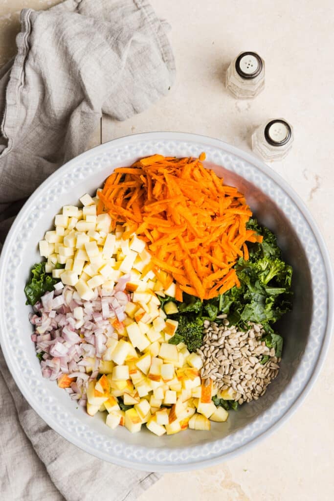 Kale, broccoli, carrots, cheese, shallot, apple and sunflower seeds in a large bowl.
