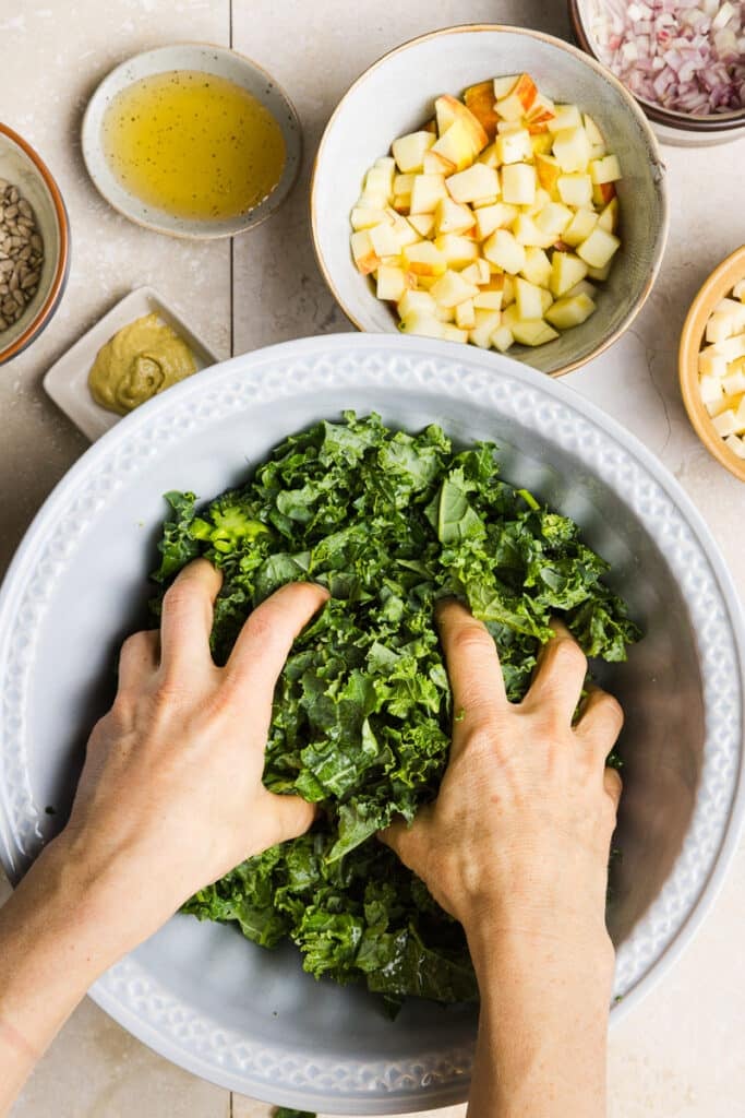 Kale in a large bowl being massaged with two hands.