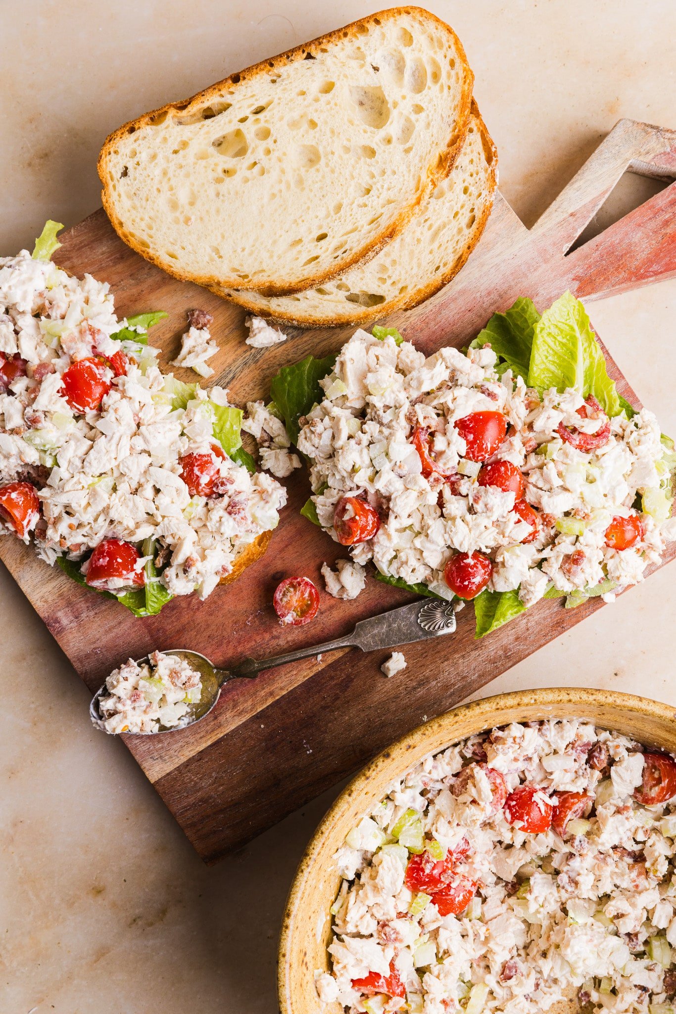 BLT chicken salad sandwiches being assembled on a wooden board.