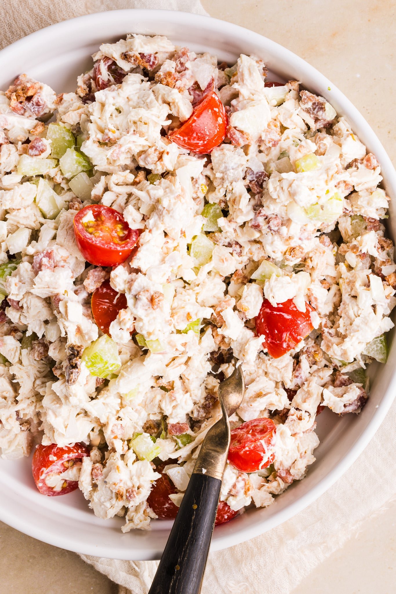 A close up shot of BLT chicken salad in a white bowl with a large spoon.