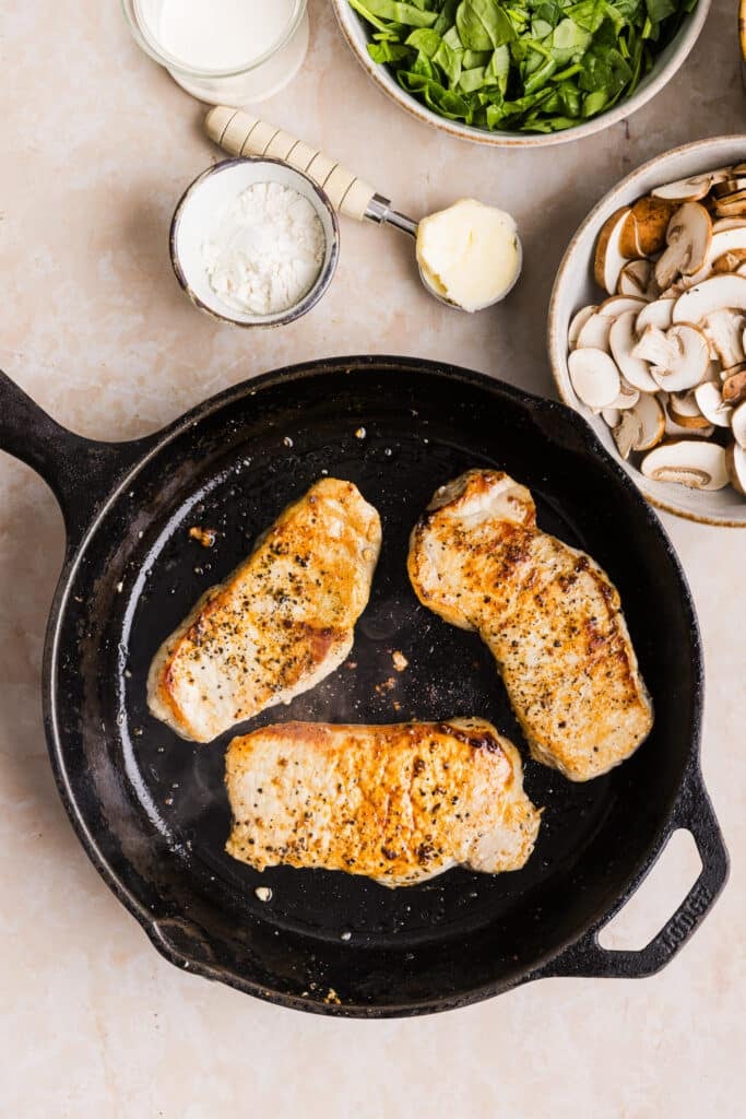 Pork chops being cooked and seared in a pan.